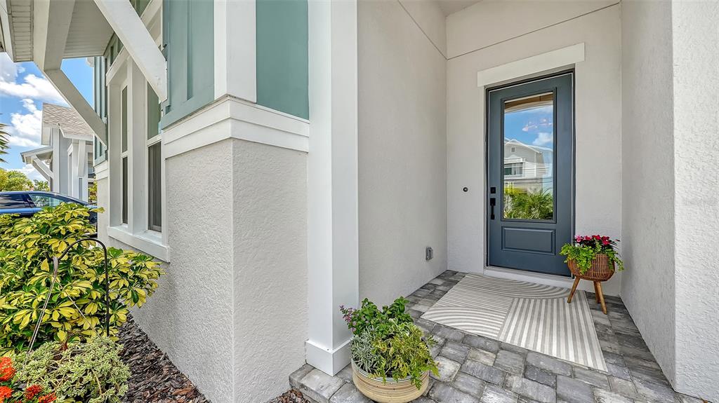 A gray front door with a glass panel sits on a paved porch with potted plants — 1578 RUNNING TIDE PLACE, SARASOTA, FL