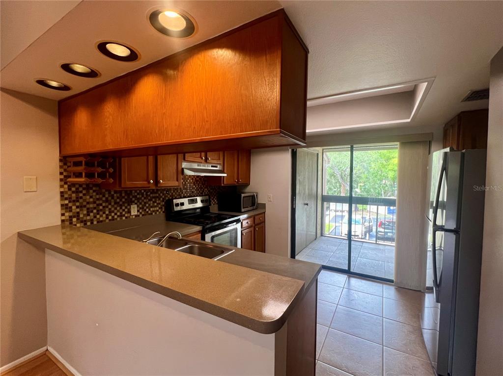 A kitchen with wooden cabinets, a breakfast bar, and a sliding glass door to a balcony — 142 WOODLAKE WYNDE UNIT 48, OLDSMAR, FL