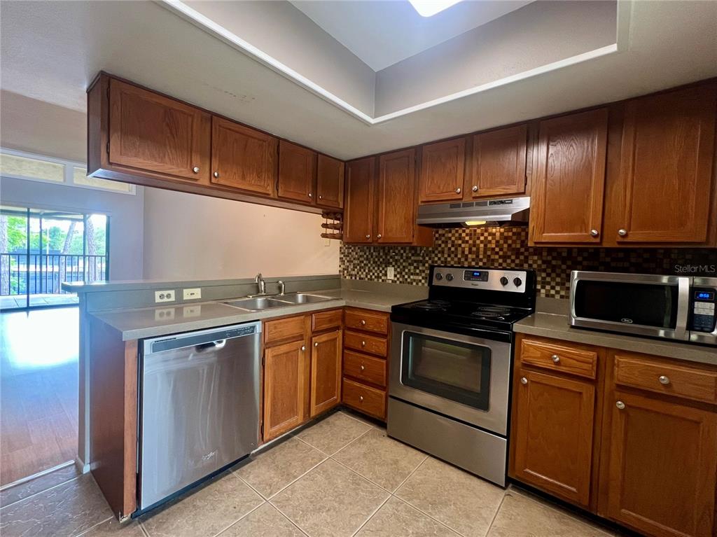 A kitchen features wood cabinets, stainless steel appliances, a tile backsplash, and tile flooring — 142 WOODLAKE WYNDE UNIT 48, OLDSMAR, FL