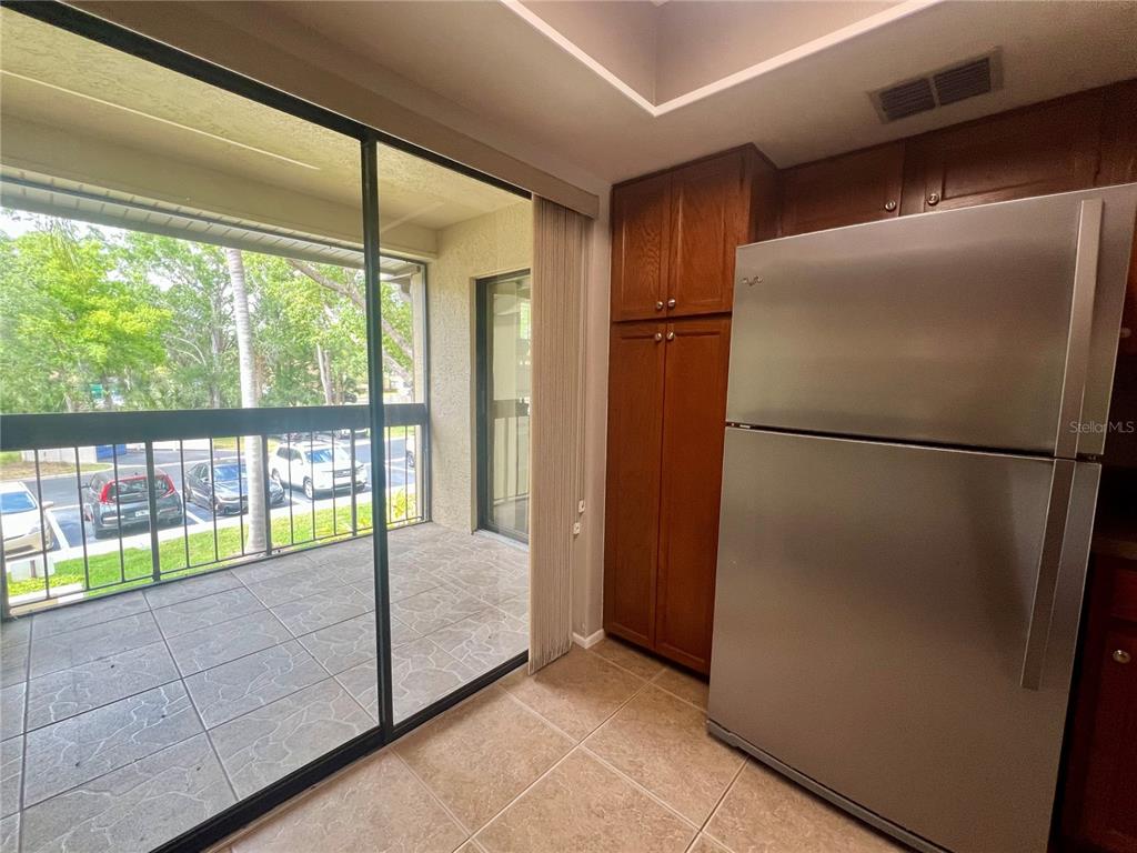 A kitchen with a stainless steel refrigerator and wood cabinets next to a screened balcony — 142 WOODLAKE WYNDE UNIT 48, OLDSMAR, FL