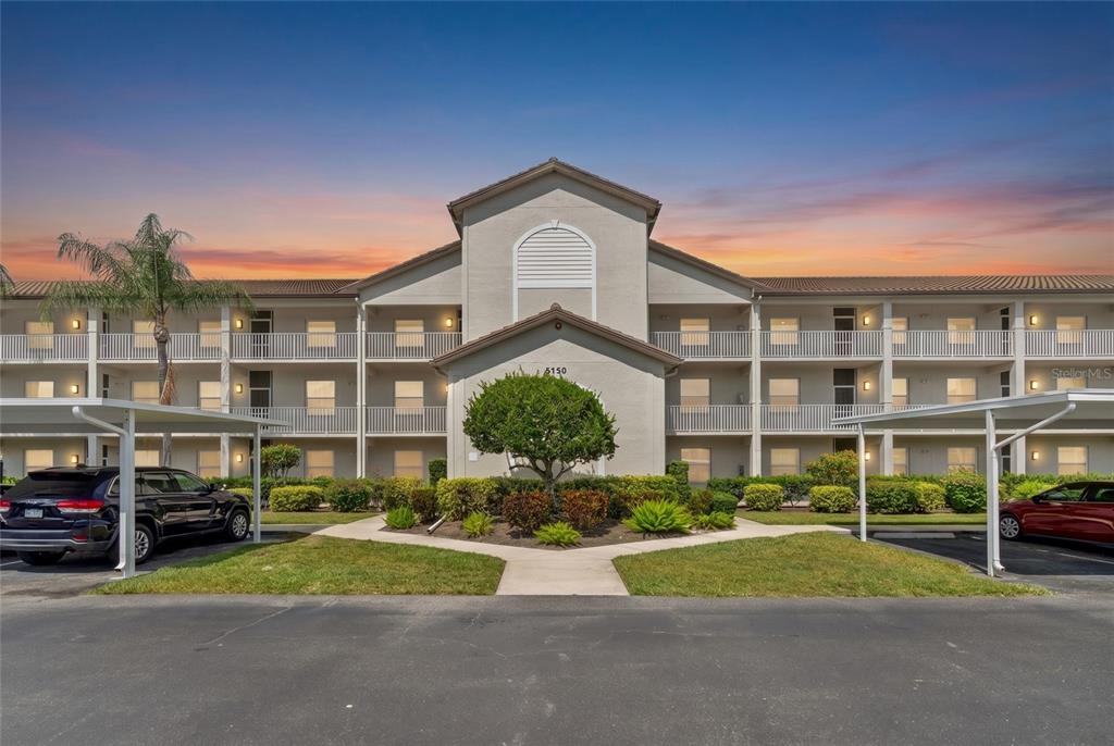 A three-story apartment building with a central entrance and covered parking spaces in front — 8750 OLDE HICKORY AVENUE UNIT 9308, SARASOTA, FL