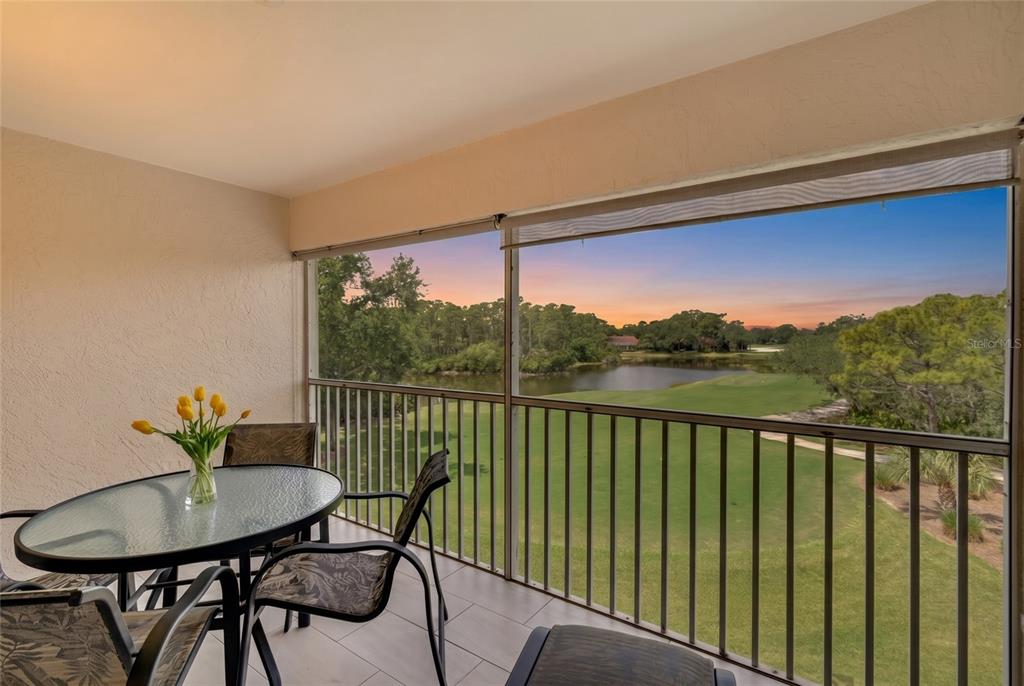 A screened-in balcony features a glass-top table, chairs, and a view of a golf course — 8750 OLDE HICKORY AVENUE UNIT 9308, SARASOTA, FL