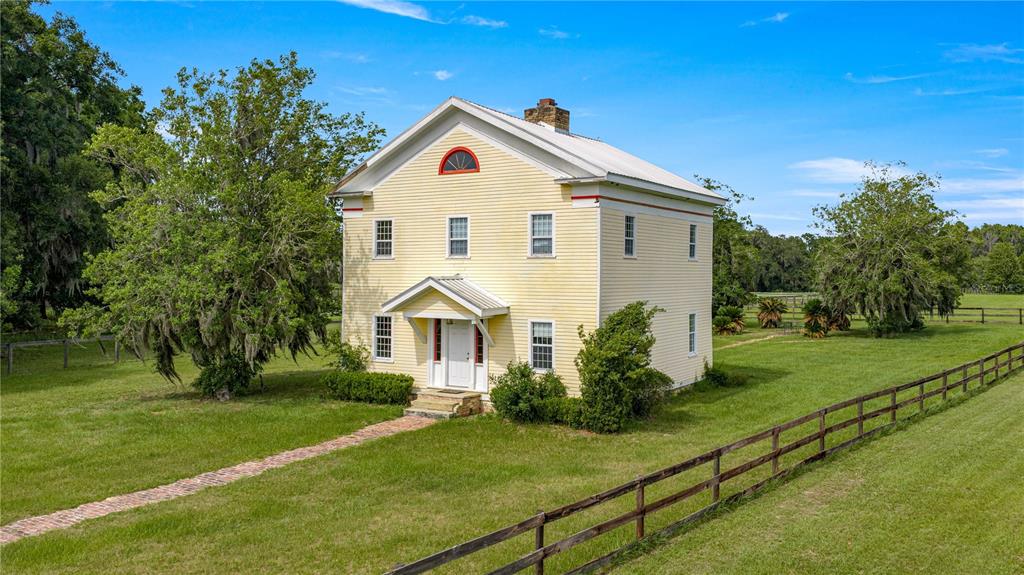 A two-story yellow farmhouse with a metal roof stands in a grassy, fenced-in field — 13939 N US HIGHWAY 441, CITRA, FL