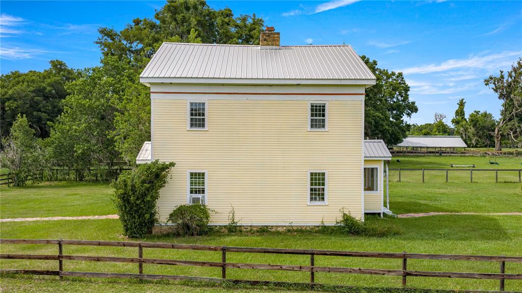 A two-story yellow farmhouse with a metal roof sits in a grassy fenced pasture — 13939 N US HIGHWAY 441, CITRA, FL