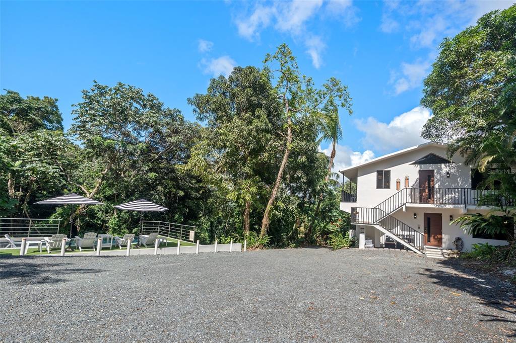 A two-story white house sits next to a gravel driveway and a fenced patio area — CARR 966 KM 2.8 BO JIMENEZ, RIO GRANDE, PR