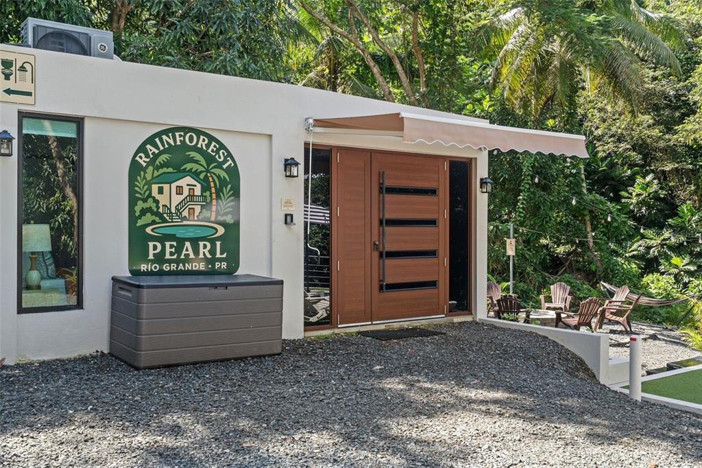 The exterior of a white building features a wooden door, a sign, and gravel ground — CARR 966 KM 2.8 BO JIMENEZ, RIO GRANDE, PR