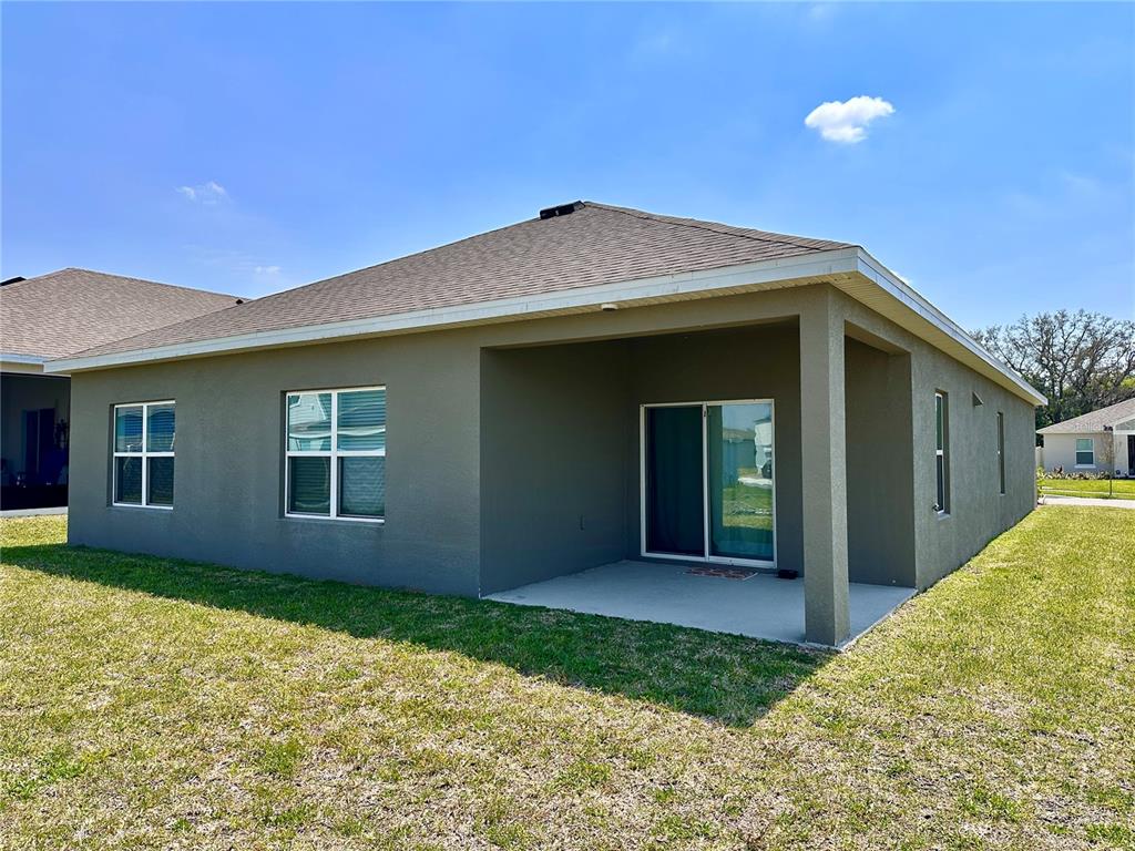 The exterior of a house features a covered patio, sliding glass doors, and a lawn — 5326 MADDIE DRIVE, HAINES CITY, FL