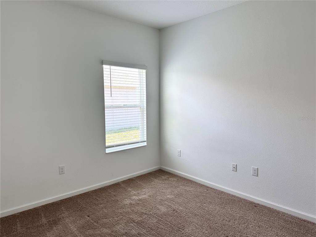 An empty bedroom features beige carpet, white walls, and a single window with blinds — 5326 MADDIE DRIVE, HAINES CITY, FL