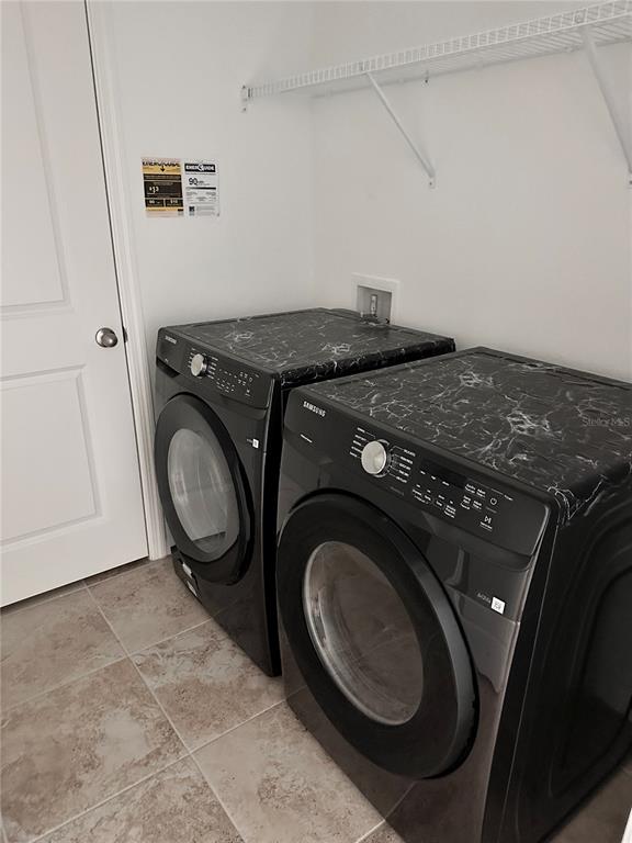 A laundry room features two black Samsung appliances with marble-patterned tops and a wire shelf — 5326 MADDIE DRIVE, HAINES CITY, FL