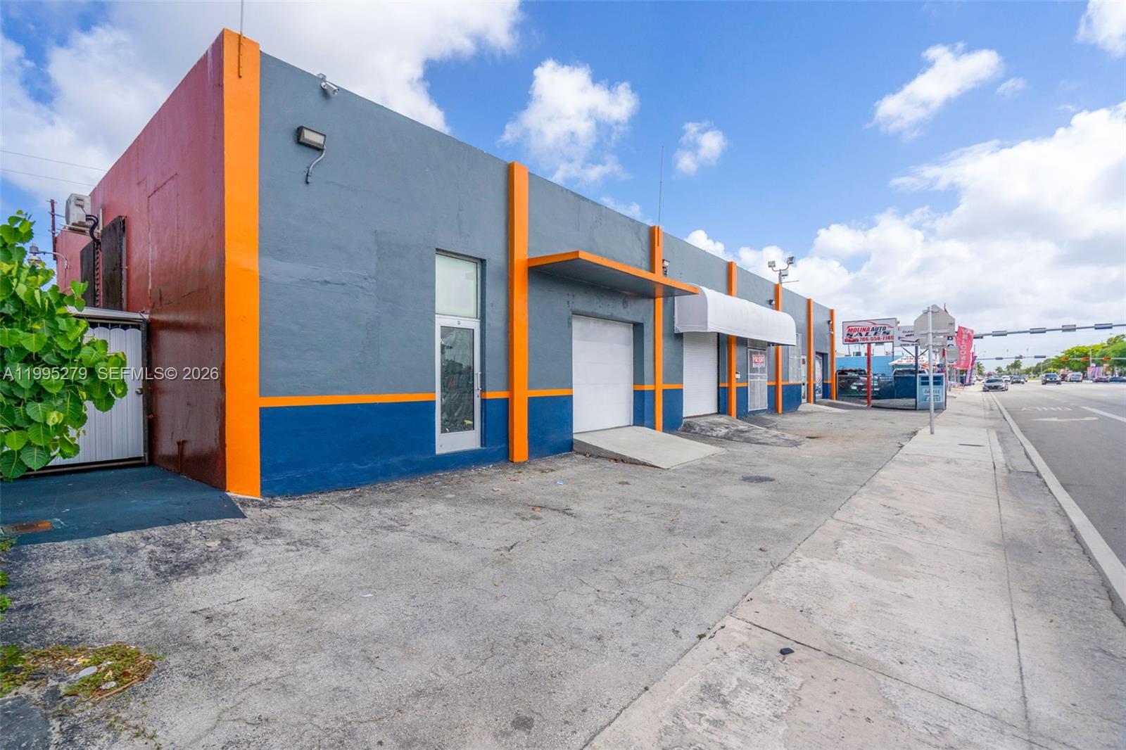 A gray and blue commercial building with orange accents features roll-up doors and a sidewalk — 4255 E 8th Ave # 3, Hialeah FL 33013, HIALEAH, FL
