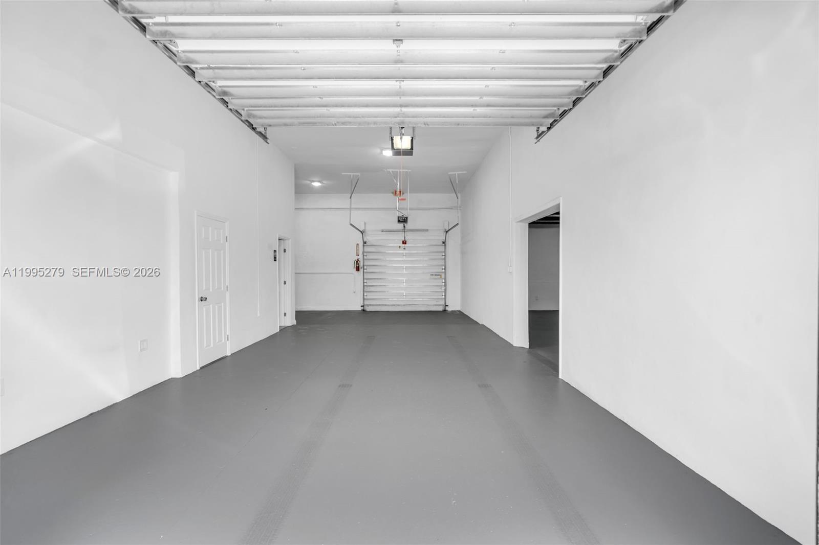 This interior view shows a spacious, empty warehouse unit with white walls, a gray floor, and a roll-up door — 4255 E 8th Ave # 3, Hialeah FL 33013, HIALEAH, FL