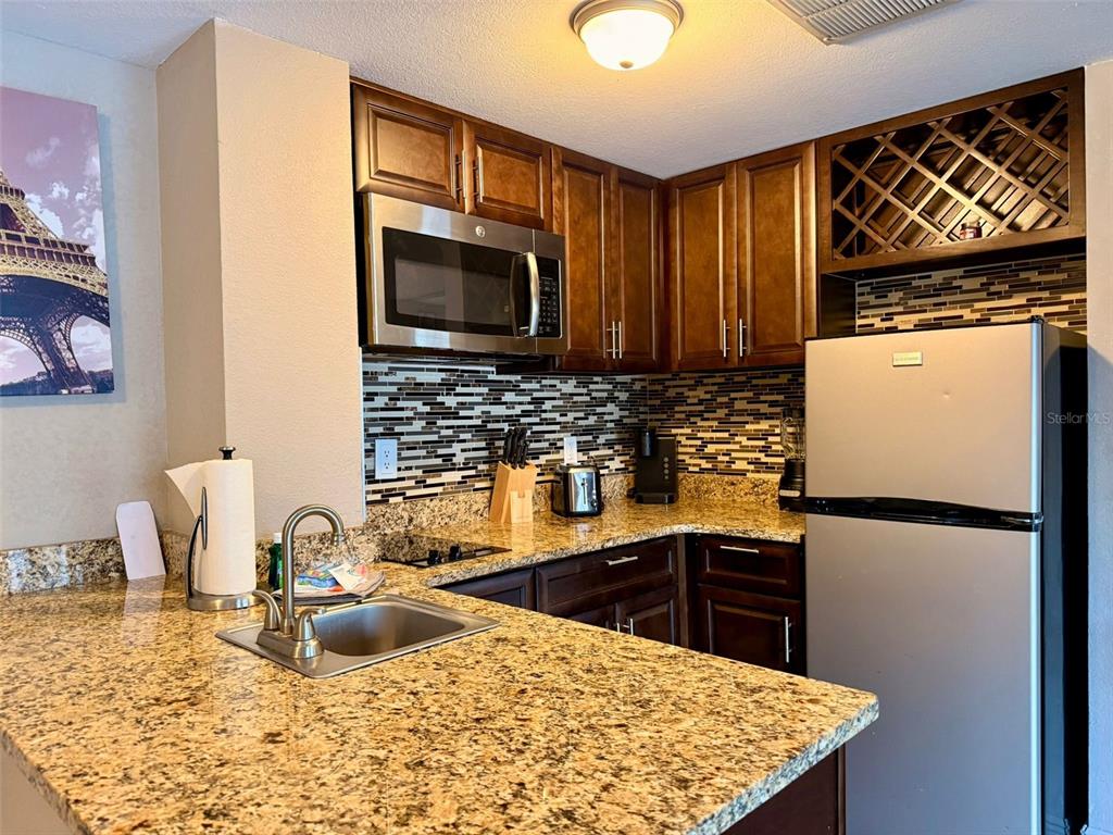 A kitchen features dark wood cabinets, granite countertops, stainless steel appliances, and a tiled backsplash — 6165 CARRIER DRIVE UNIT 2203, ORLANDO, FL