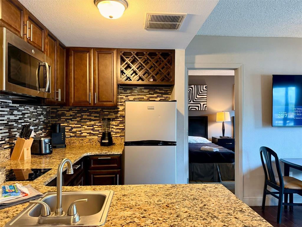 A kitchen with dark wood cabinets, granite countertops, and a stainless steel refrigerator — 6165 CARRIER DRIVE UNIT 2203, ORLANDO, FL