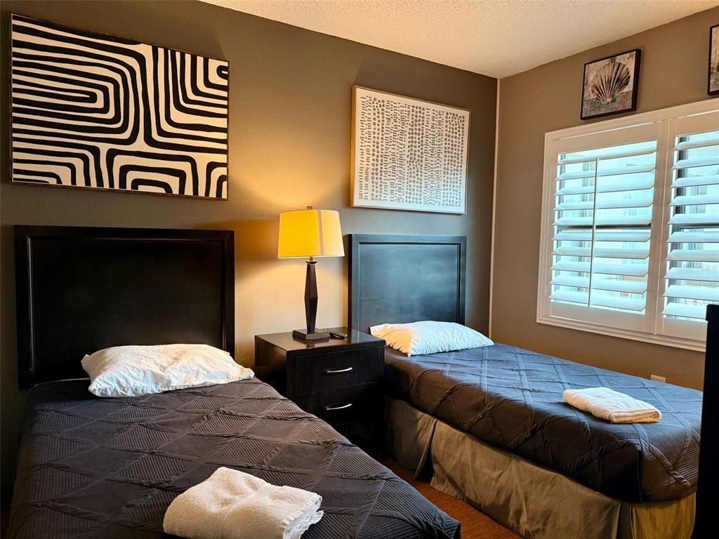 A bedroom features two twin beds with dark bedding, a nightstand, and wall art — 6165 CARRIER DRIVE UNIT 2203, ORLANDO, FL