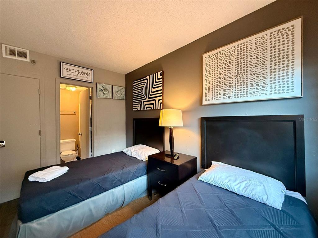 A bedroom features two twin beds, a shared nightstand with a lamp, and an attached bathroom — 6165 CARRIER DRIVE UNIT 2203, ORLANDO, FL