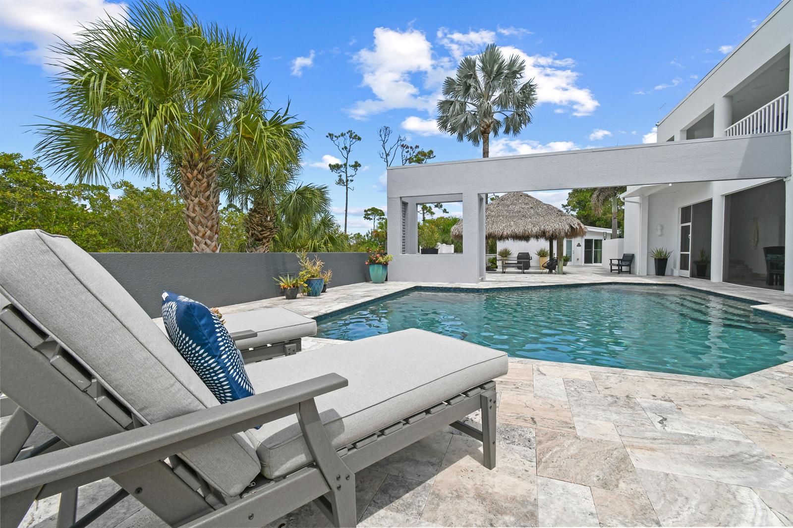 A swimming pool sits on a stone patio next to lounge chairs and a house — 10561 SE Le Parc, Jupiter FL 33469, JUPITER, FL