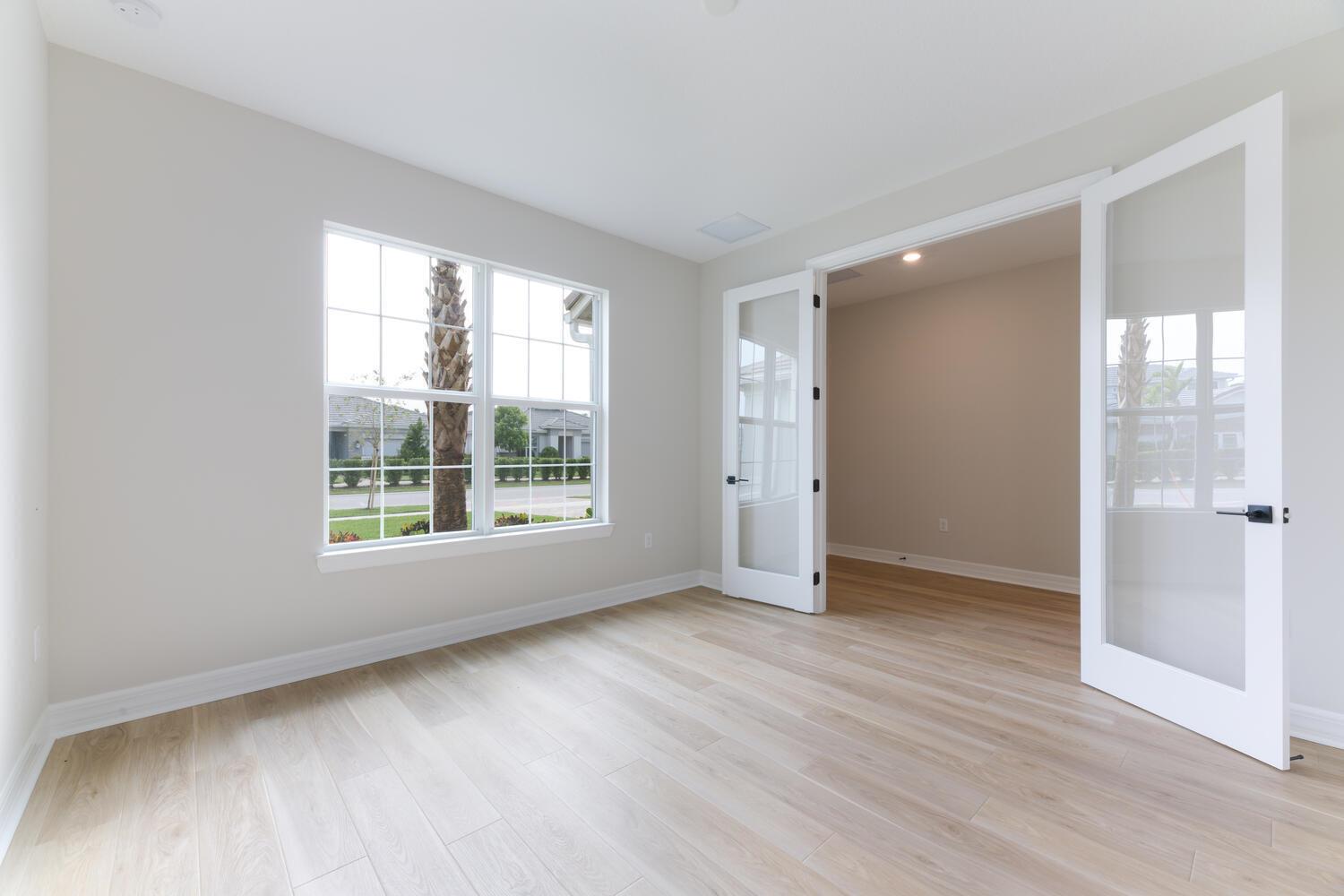 An empty room with light wood flooring, a window, and white French doors — 9677 Mosler Trail, Lake Worth FL 33467, LAKE WORTH, FL