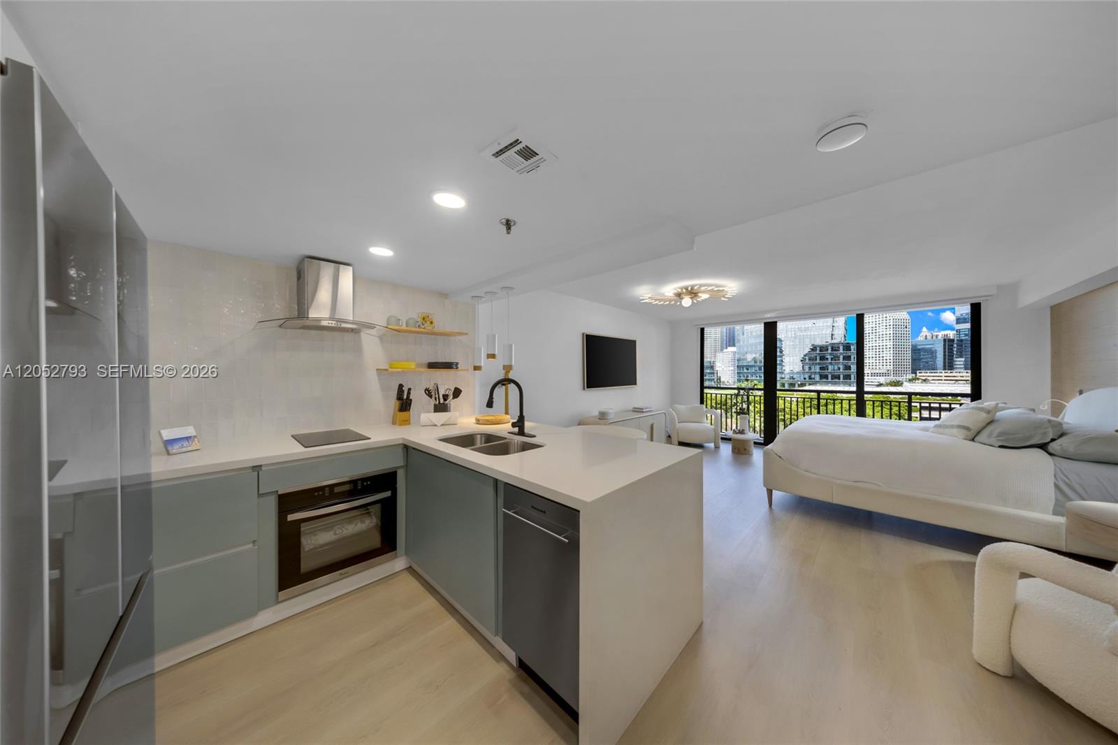 A modern studio apartment features a kitchen with light blue cabinets and a bedroom area — 540 Brickell Key Dr # 809, Miami FL 33131, MIAMI, FL