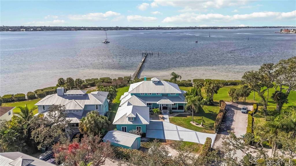 An aerial view shows two coastal houses with metal roofs situated along a waterfront dock — 2207 5TH STREET W, PALMETTO, FL