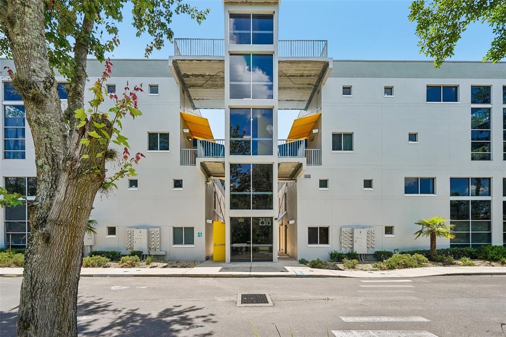 A modern multi-story apartment building features a central glass stairwell and yellow balcony awnings — 2515 SW 35TH PLACE UNIT 103, GAINESVILLE, FL