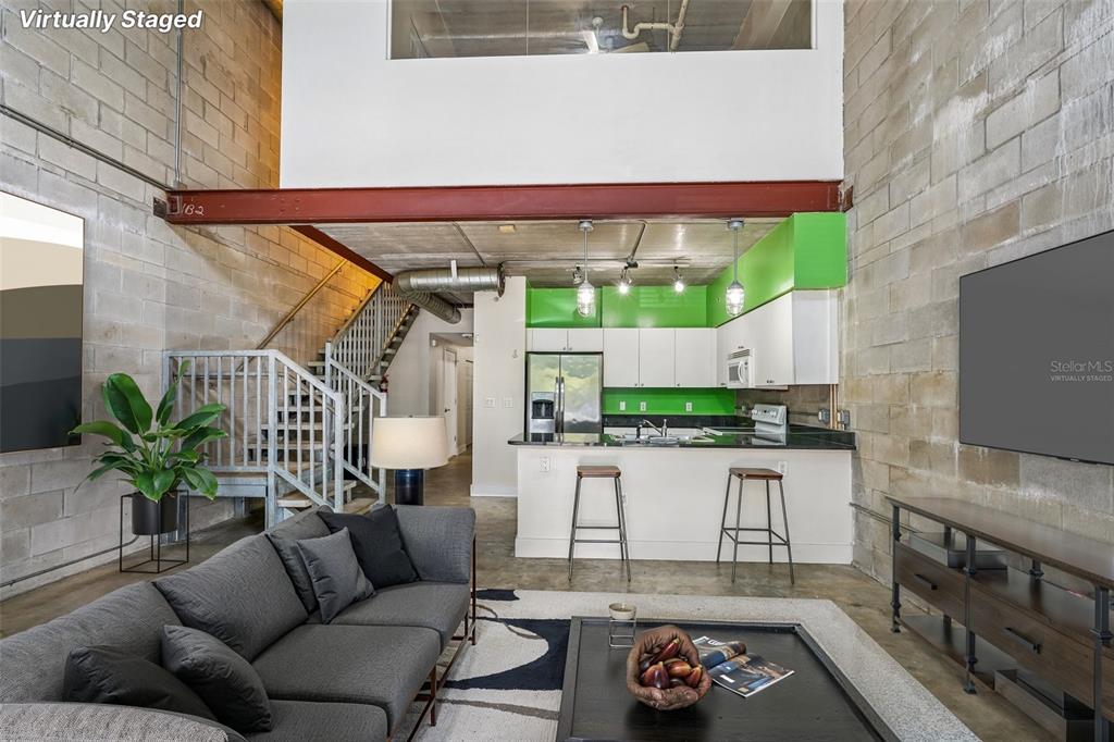 A living room and kitchen area with concrete block walls, a metal staircase, and loft — 2515 SW 35TH PLACE UNIT 103, GAINESVILLE, FL