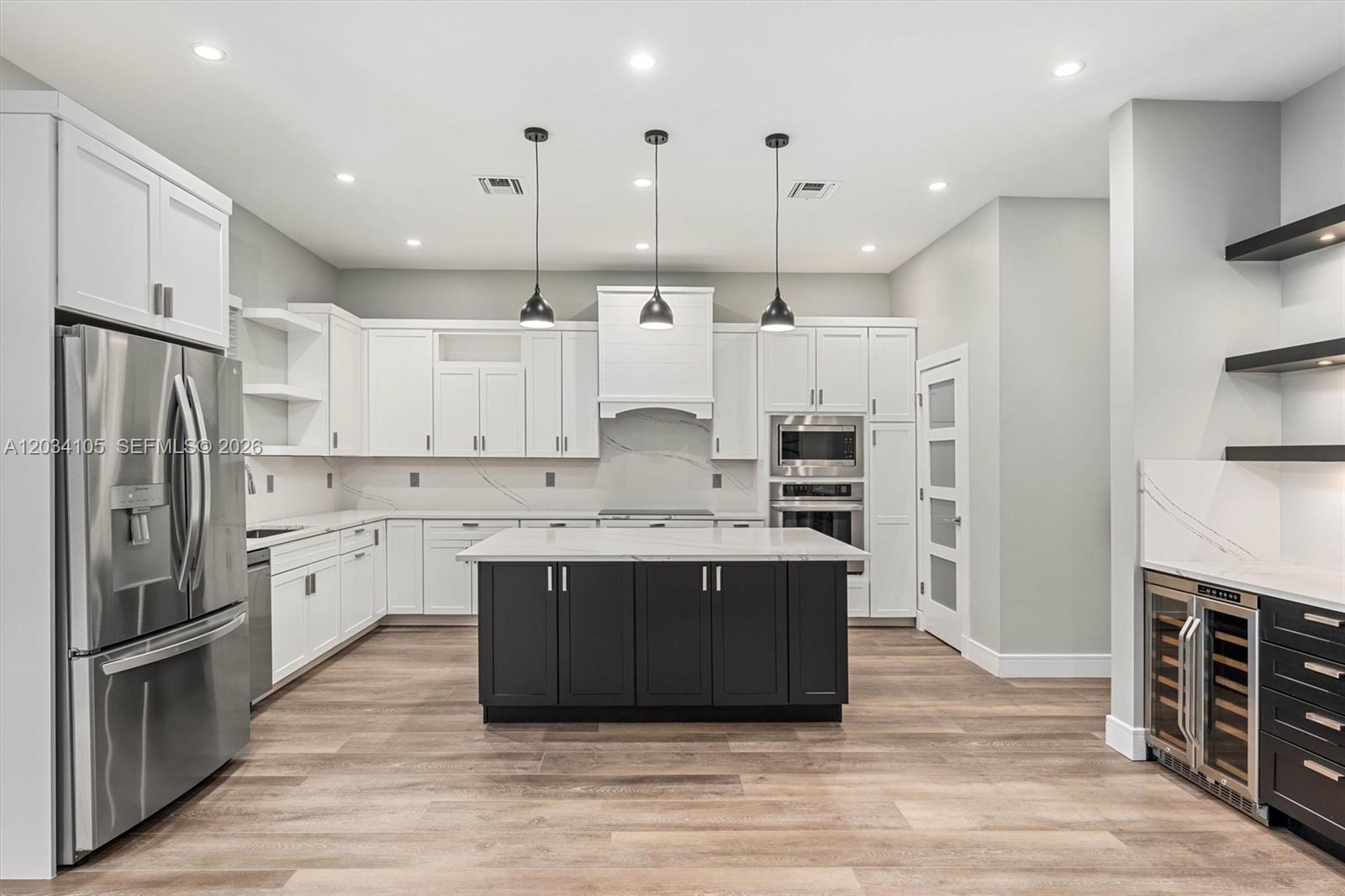 A modern kitchen features white cabinets, a dark island, stainless appliances, and wood-look flooring — 2431 NE 20th Ave, Lighthouse Point FL 33064, LIGHTHOUSE POINT, FL