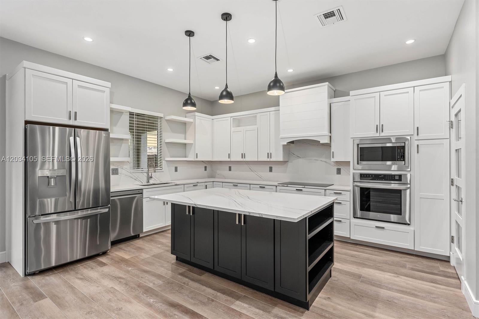 A modern kitchen features white cabinetry, a dark island, stainless steel appliances, and marble countertops — 2431 NE 20th Ave, Lighthouse Point FL 33064, LIGHTHOUSE POINT, FL