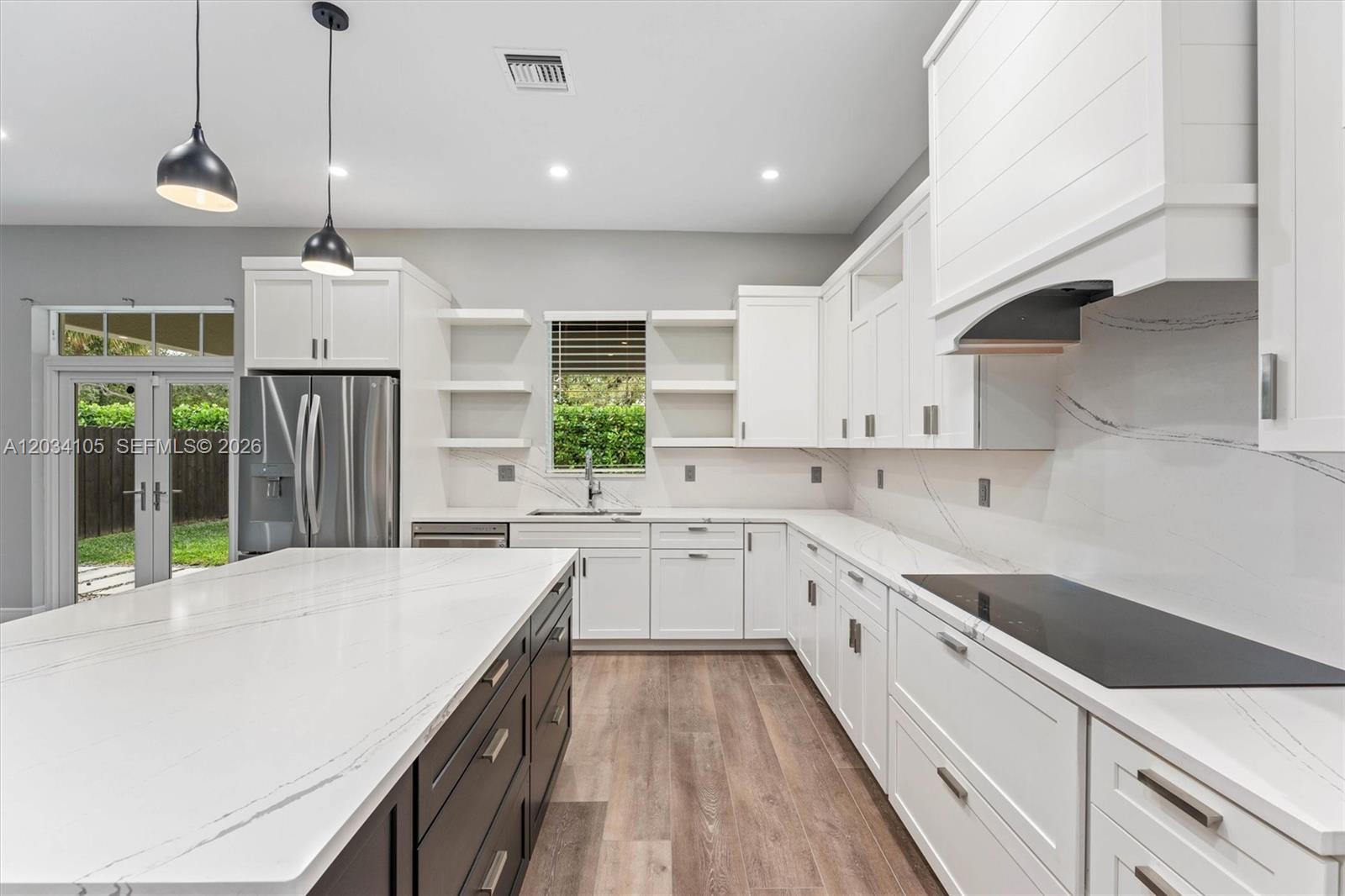 A modern kitchen features white cabinetry, a dark island, marble-look countertops, and stainless steel appliances — 2431 NE 20th Ave, Lighthouse Point FL 33064, LIGHTHOUSE POINT, FL