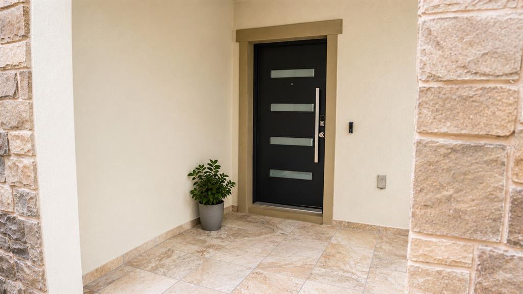 A modern black front door with horizontal glass panels sits under a covered stone entryway — 2824 NOBLE CROW DRIVE, KISSIMMEE, FL