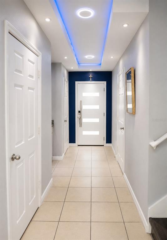 A hallway with tile flooring, white doors, and a blue-lit ceiling leads to an entrance — 2824 NOBLE CROW DRIVE, KISSIMMEE, FL