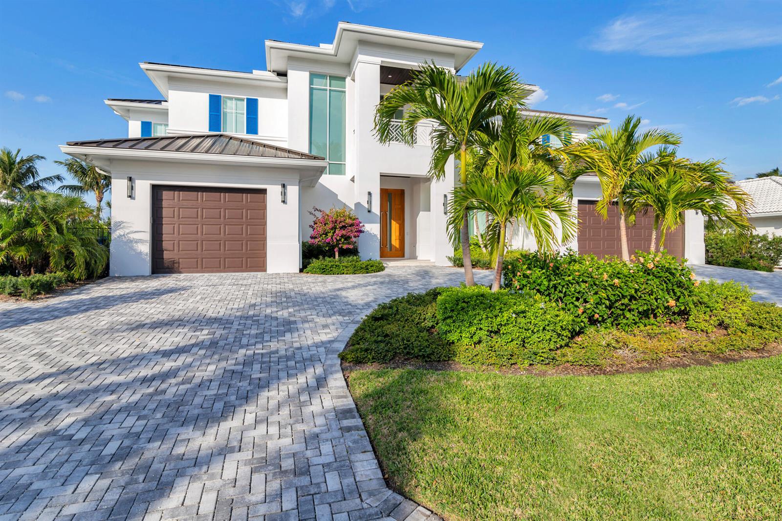 A two-story white house with a paver driveway, two brown garage doors, and palm trees — 1180 Bimini Lane, Singer Island FL 33404, SINGER ISLAND, FL