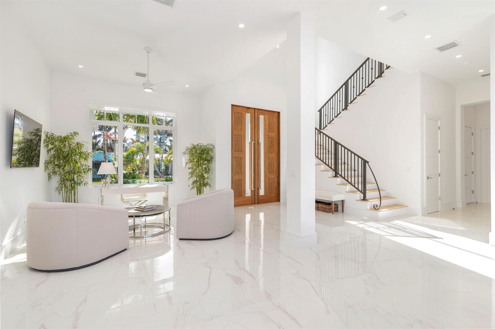 A bright foyer features white marble floors, a wooden double door, and a black staircase — 1180 Bimini Lane, Singer Island FL 33404, SINGER ISLAND, FL