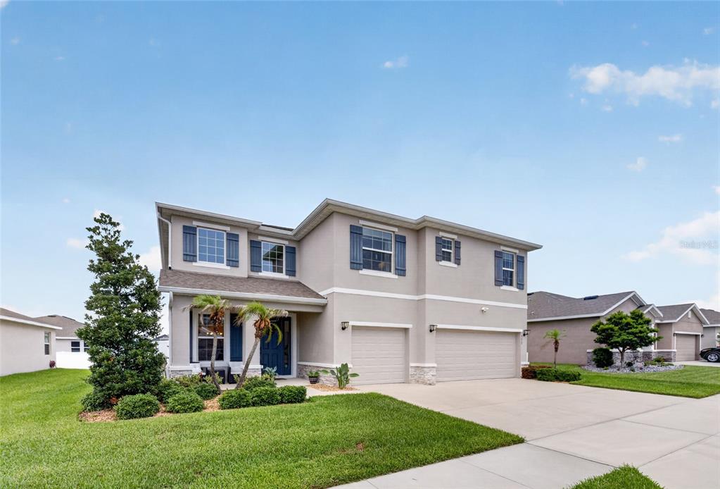 A two-story suburban house with a beige stucco exterior, blue shutters, and a three-car garage — 5859 SW 82ND LANE, OCALA, FL