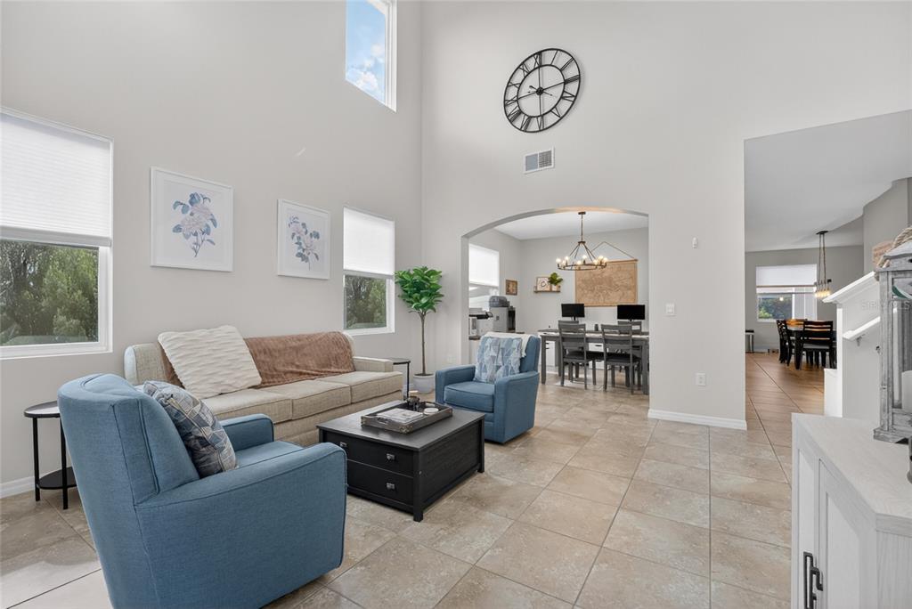 A living room with high ceilings, tile floors, blue armchairs, and an adjacent dining area — 5859 SW 82ND LANE, OCALA, FL