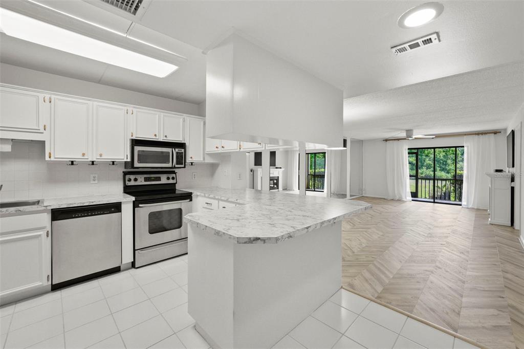 A kitchen with white cabinets and marble-look countertops opens to a living area with flooring — 1200 TARPON WOODS BOULEVARD UNIT Q4, PALM HARBOR, FL