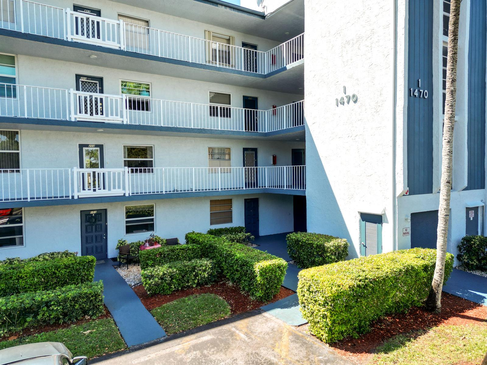 A four-story apartment building exterior features white balconies, dark blue doors, and manicured landscaping — 1470 NW 80th Avenue # 204, Margate FL 33063, MARGATE, FL