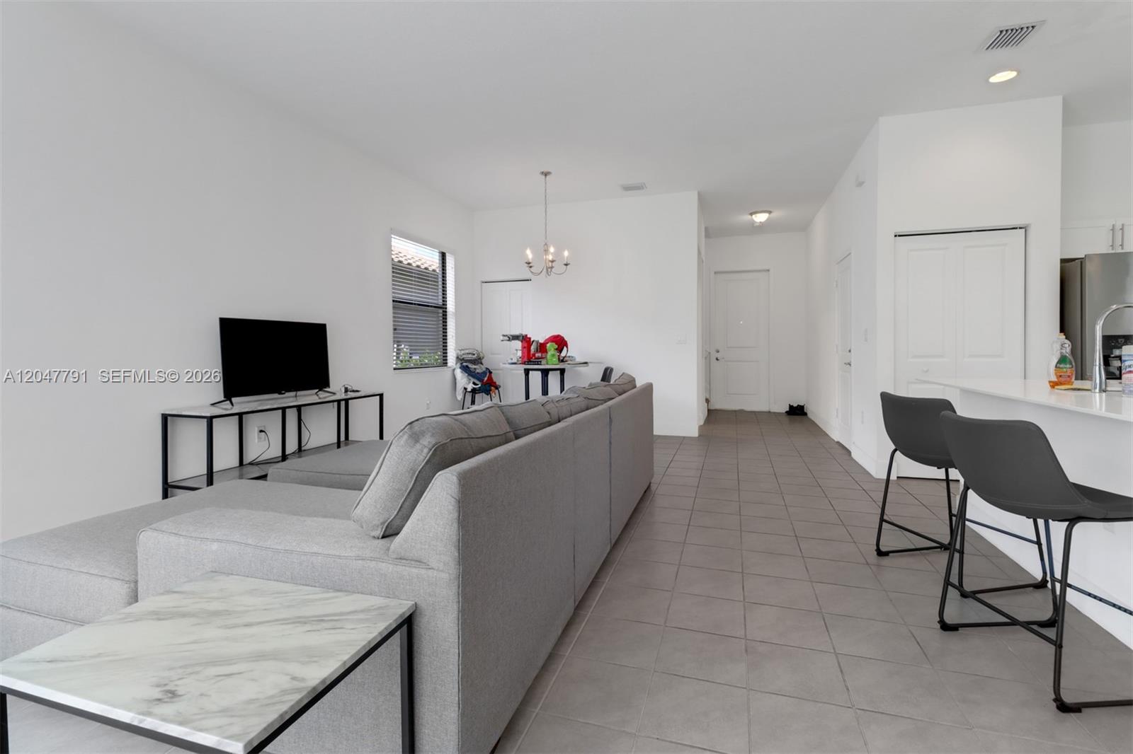 An open-concept living area features a gray sectional sofa, tile flooring, and a kitchen island — 5504 Agostino Way, Ave Maria FL 34142, AVE MARIA, FL