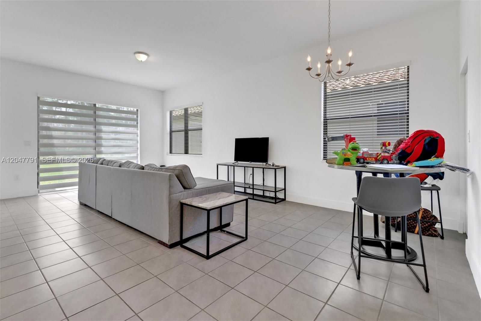 A living room features a gray sectional sofa, a television console, and a dining area — 5504 Agostino Way, Ave Maria FL 34142, AVE MARIA, FL