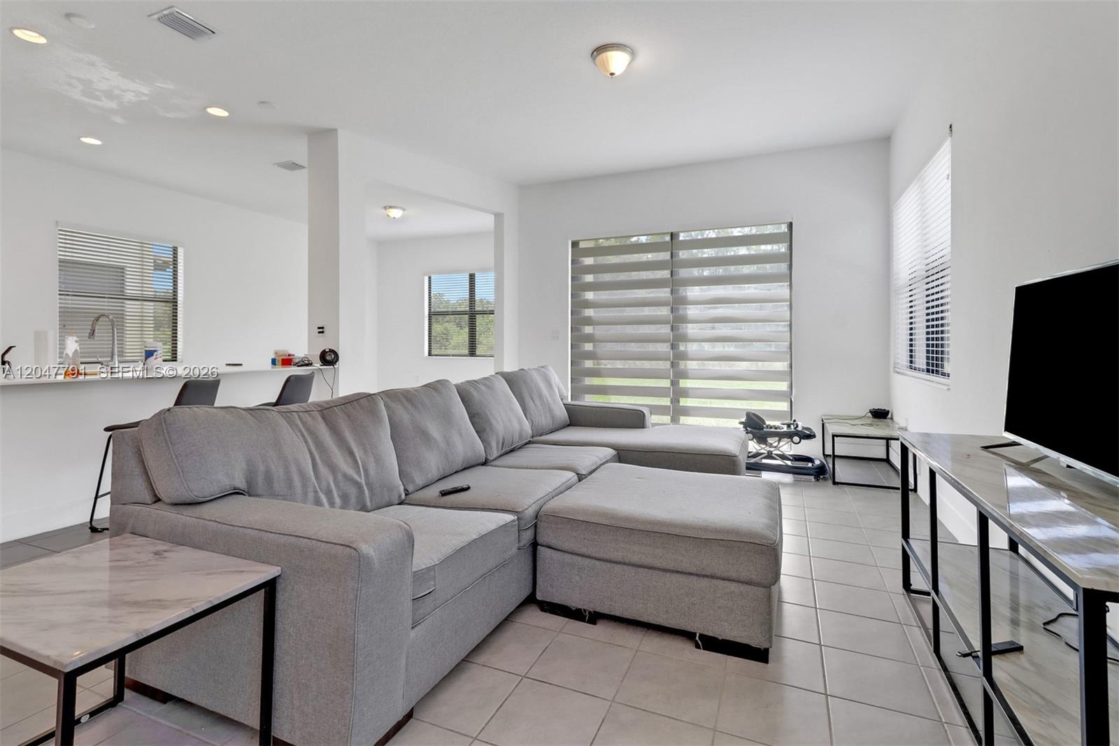 A living room features a gray sectional sofa, tile flooring, and a television on a stand — 5504 Agostino Way, Ave Maria FL 34142, AVE MARIA, FL