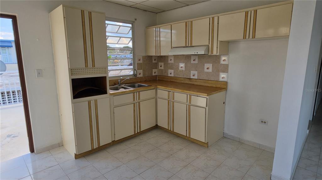 A kitchen features off-white cabinets with vertical wood trim, tiled backsplash, and light-colored floor tiles — CALLE 6, G-27 URB FRANCISCO OLLER UNIT 2, BAYAMON, PR