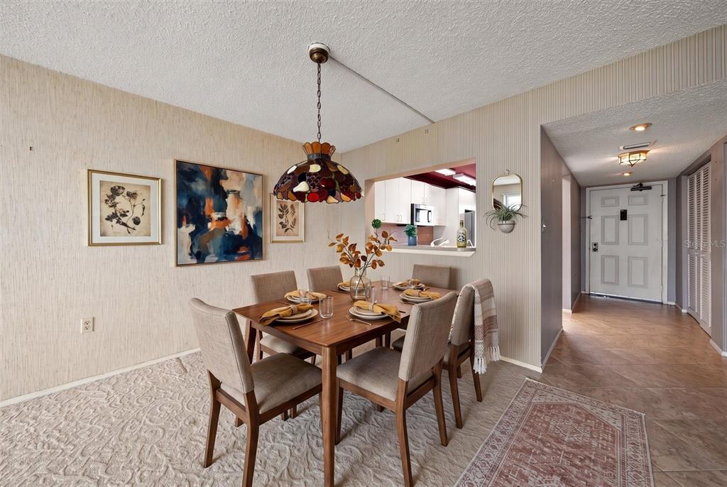 A dining room with a wooden table, chairs, stained-glass pendant light, and a kitchen pass-through — 1250 GULF BOULEVARD UNIT 706, CLEARWATER BEACH, FL