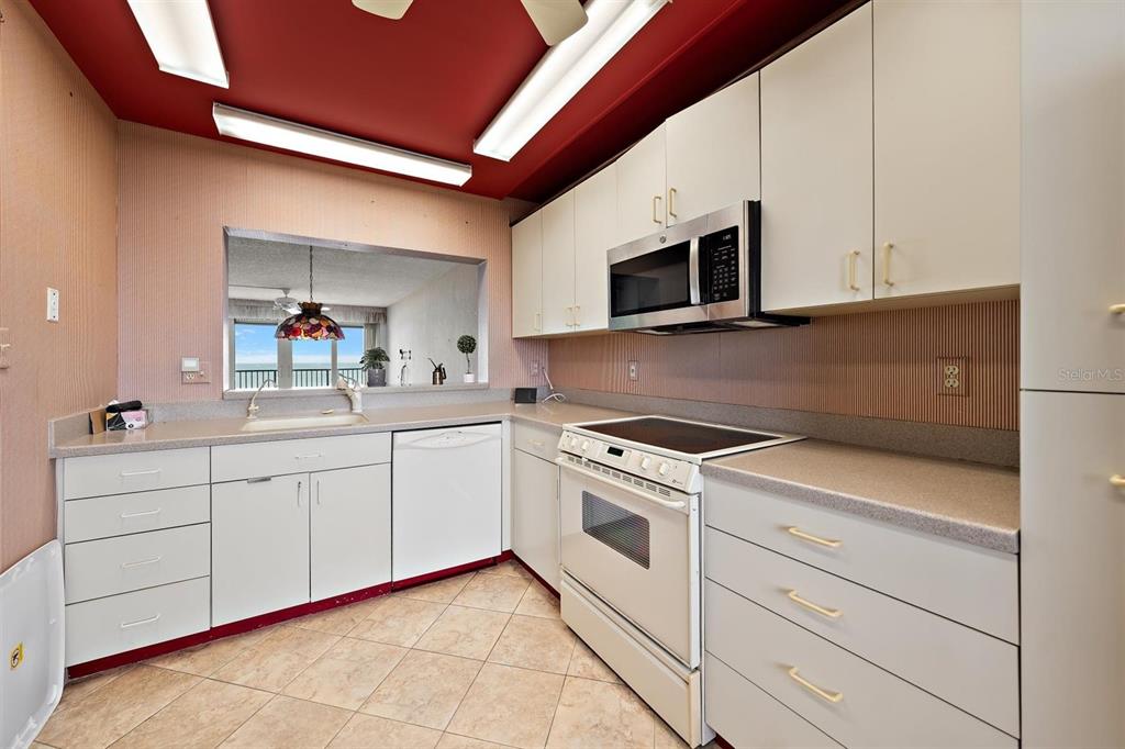 A kitchen features white cabinets, a microwave, a stove, and a pass-through window to outside — 1250 GULF BOULEVARD UNIT 706, CLEARWATER BEACH, FL