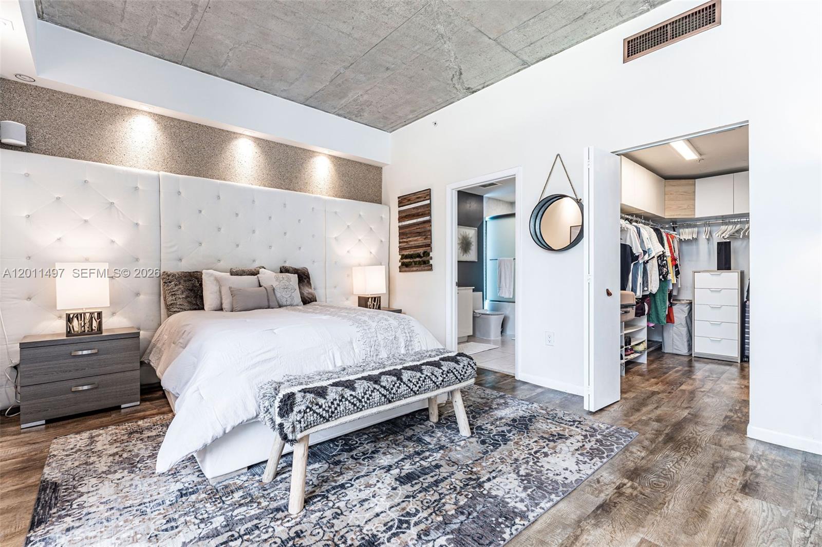 A bedroom features a tufted headboard, concrete ceiling, patterned rug, and an attached walk-in closet — 133 NE 2nd Ave # 1208, Miami FL 33132, MIAMI, FL