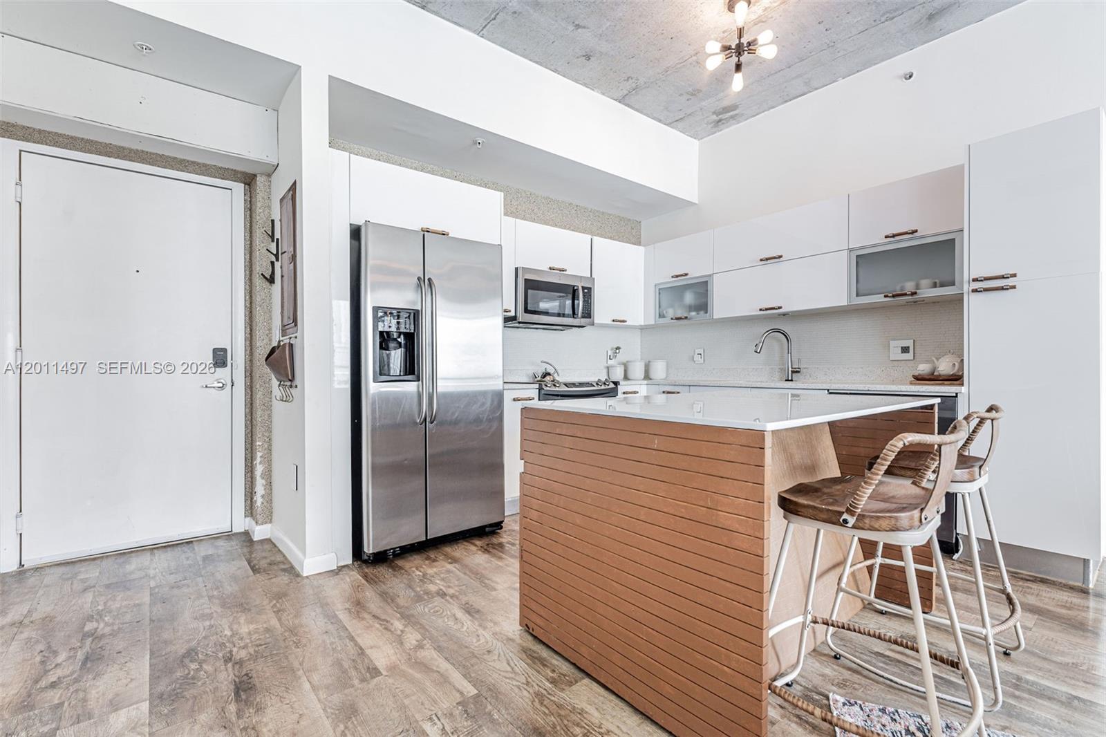 A modern kitchen features stainless steel appliances, white cabinetry, and a slatted wood kitchen island — 133 NE 2nd Ave # 1208, Miami FL 33132, MIAMI, FL