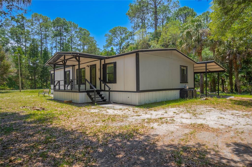 A single-story manufactured home with a covered front porch and a side carport — 6550 SE DEBRA AVENUE, INGLIS, FL