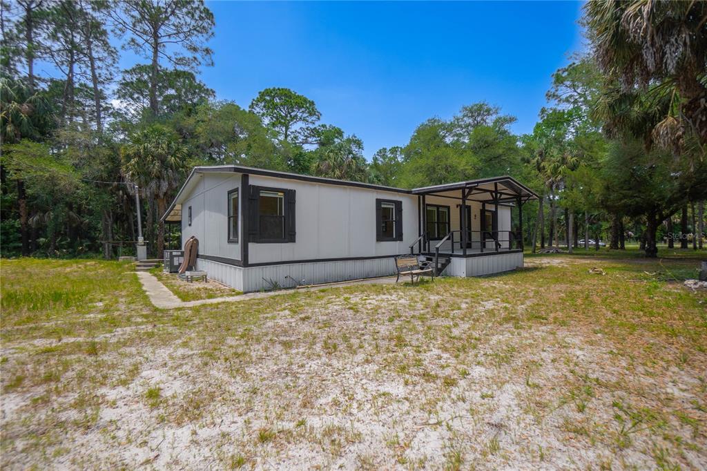 A single-story manufactured home with a covered front porch sits on a sandy, wooded lot — 6550 SE DEBRA AVENUE, INGLIS, FL