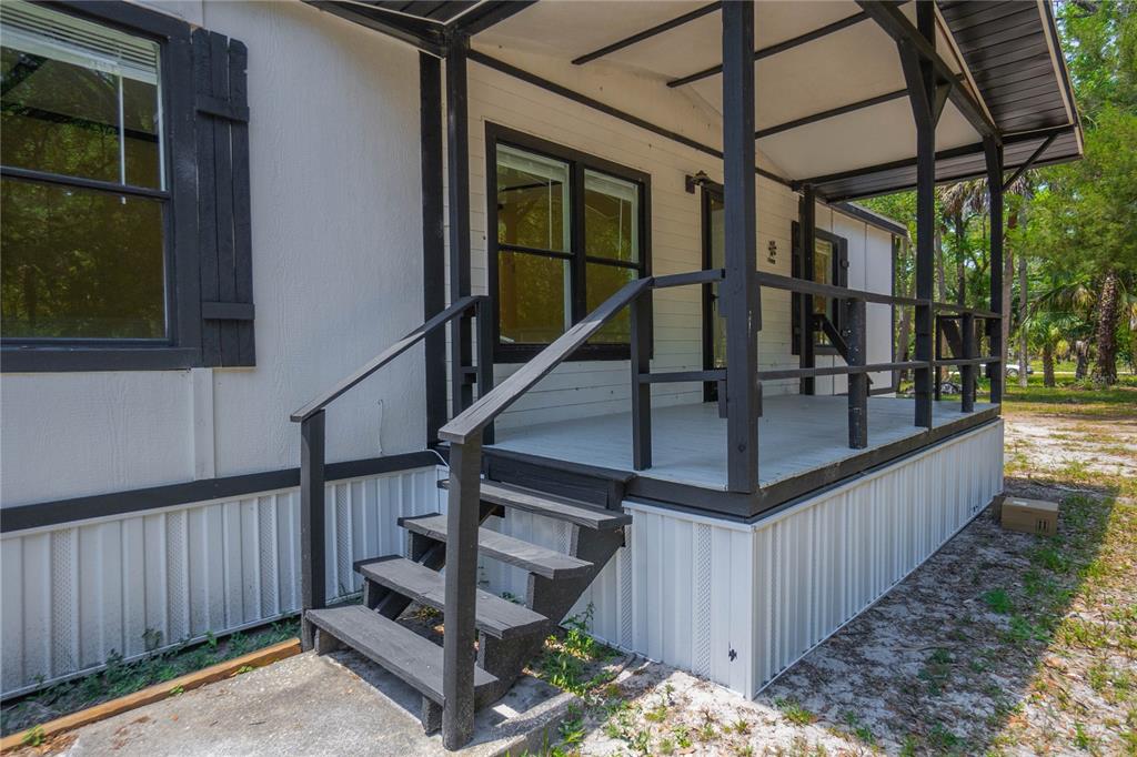 A white mobile home features a covered wooden porch with black railings and stairs — 6550 SE DEBRA AVENUE, INGLIS, FL