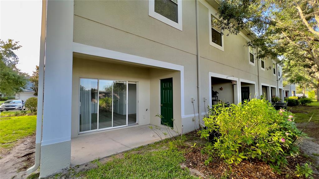 A beige multi-story townhouse exterior features a ground-level concrete patio with sliding glass doors — 10946 SAVANNAH WOOD DRIVE UNIT 147, ORLANDO, FL