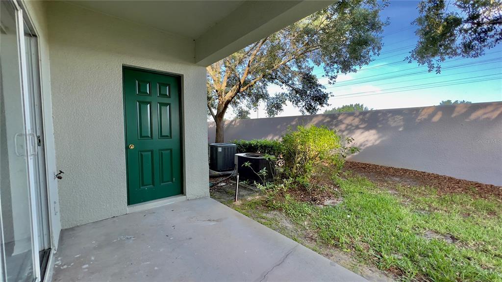 A concrete patio features a green door, two air conditioning units, and a privacy wall — 10946 SAVANNAH WOOD DRIVE UNIT 147, ORLANDO, FL