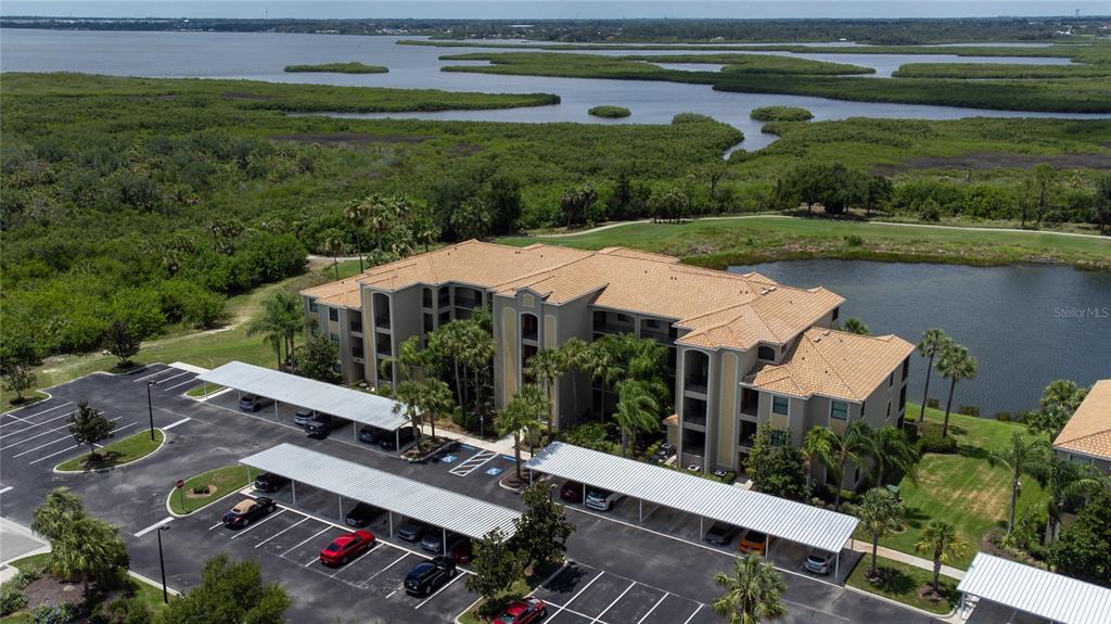 An aerial view shows a multi-story apartment building with covered parking and a nearby pond — 7005 RIVER HAMMOCK DRIVE UNIT 202, BRADENTON, FL